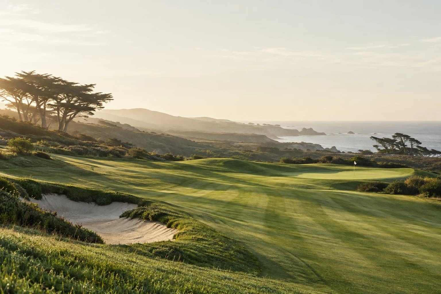 Morning sunlight across a coastal golf course, cypress trees and the ocean beyond.